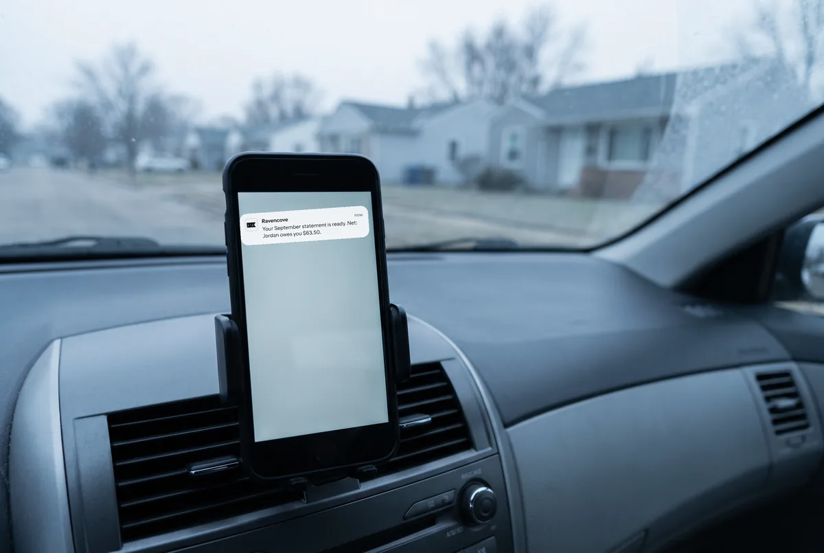 A phone on a car dashboard showing a Ravencove alert that the September statement is ready.